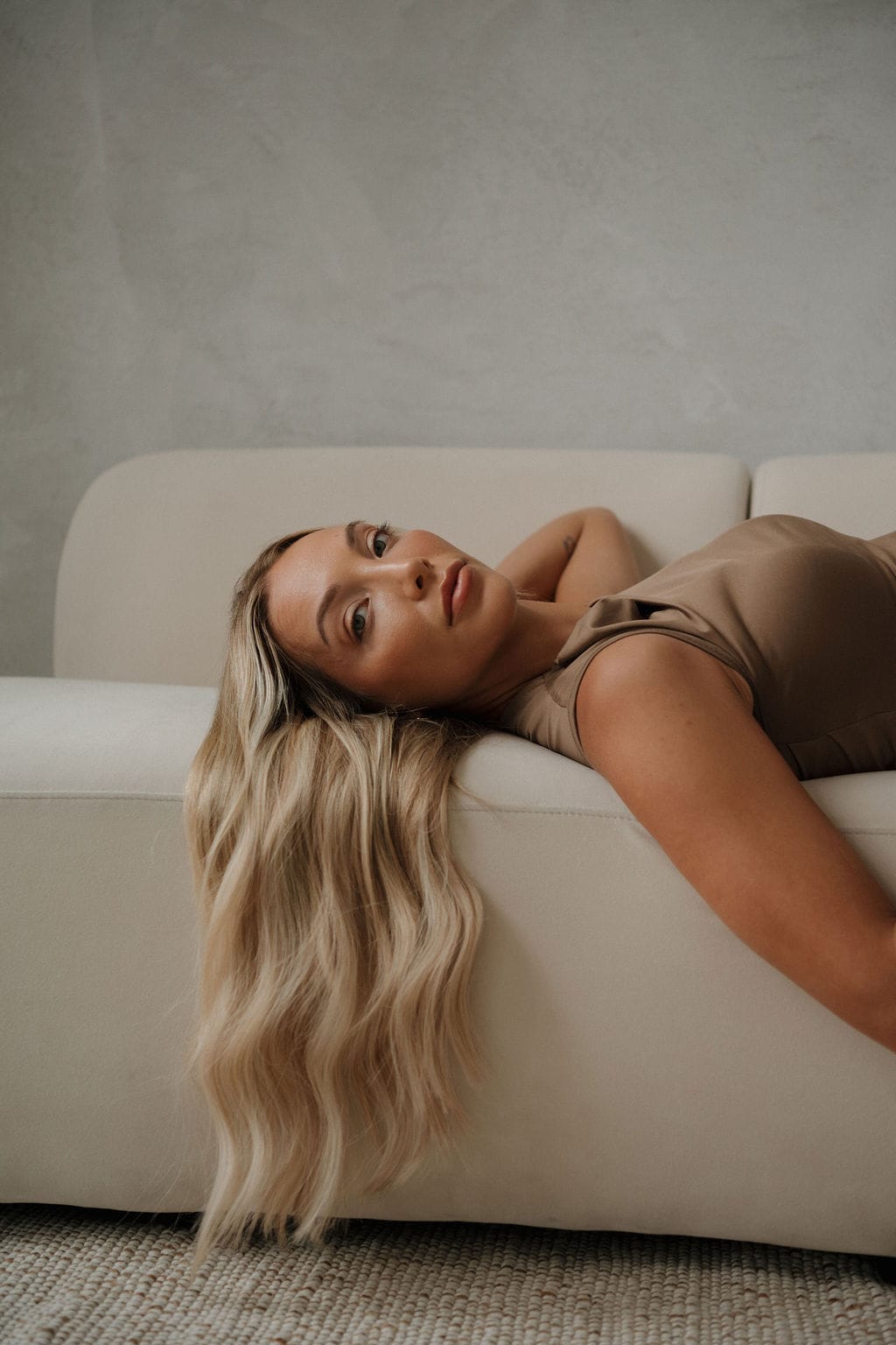 A model lying back on a sofa, her long blonde wefts falling over the edge